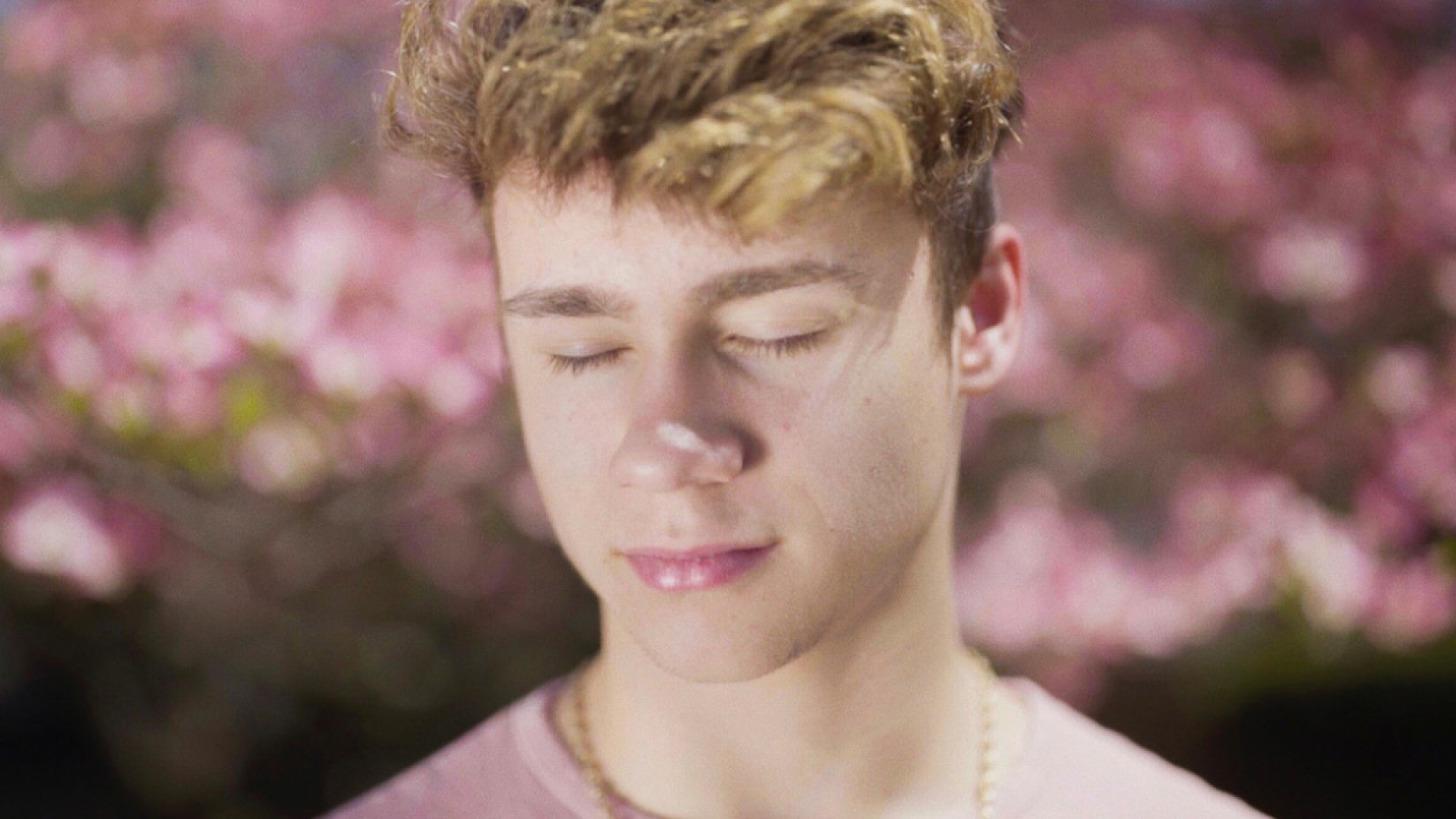 eng: Close-up of a beautiful curly young man with closed eyes on a background of pink flowers