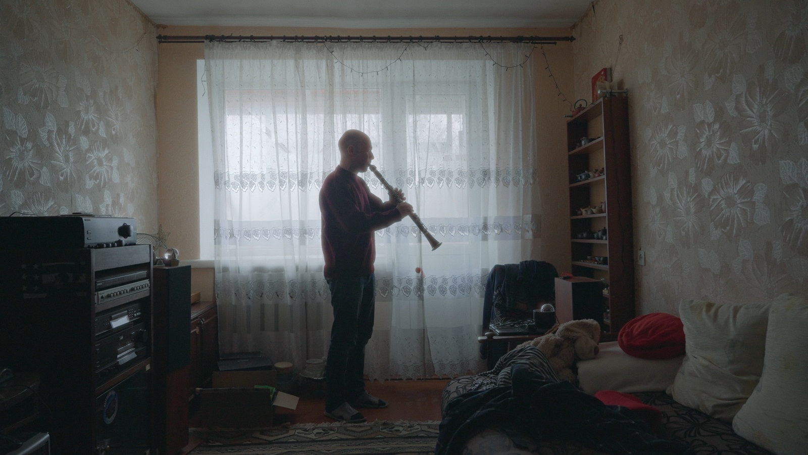rus: Чоловік стоїть посеред кімнати та грає на кларнеті.