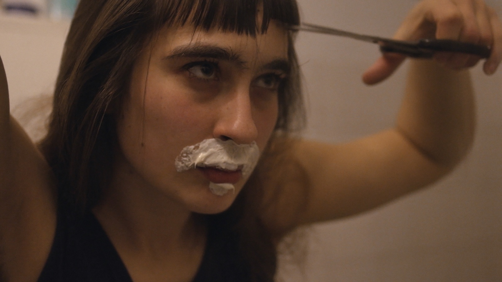 eng: A young woman with a foam mustache cuts her bangs.