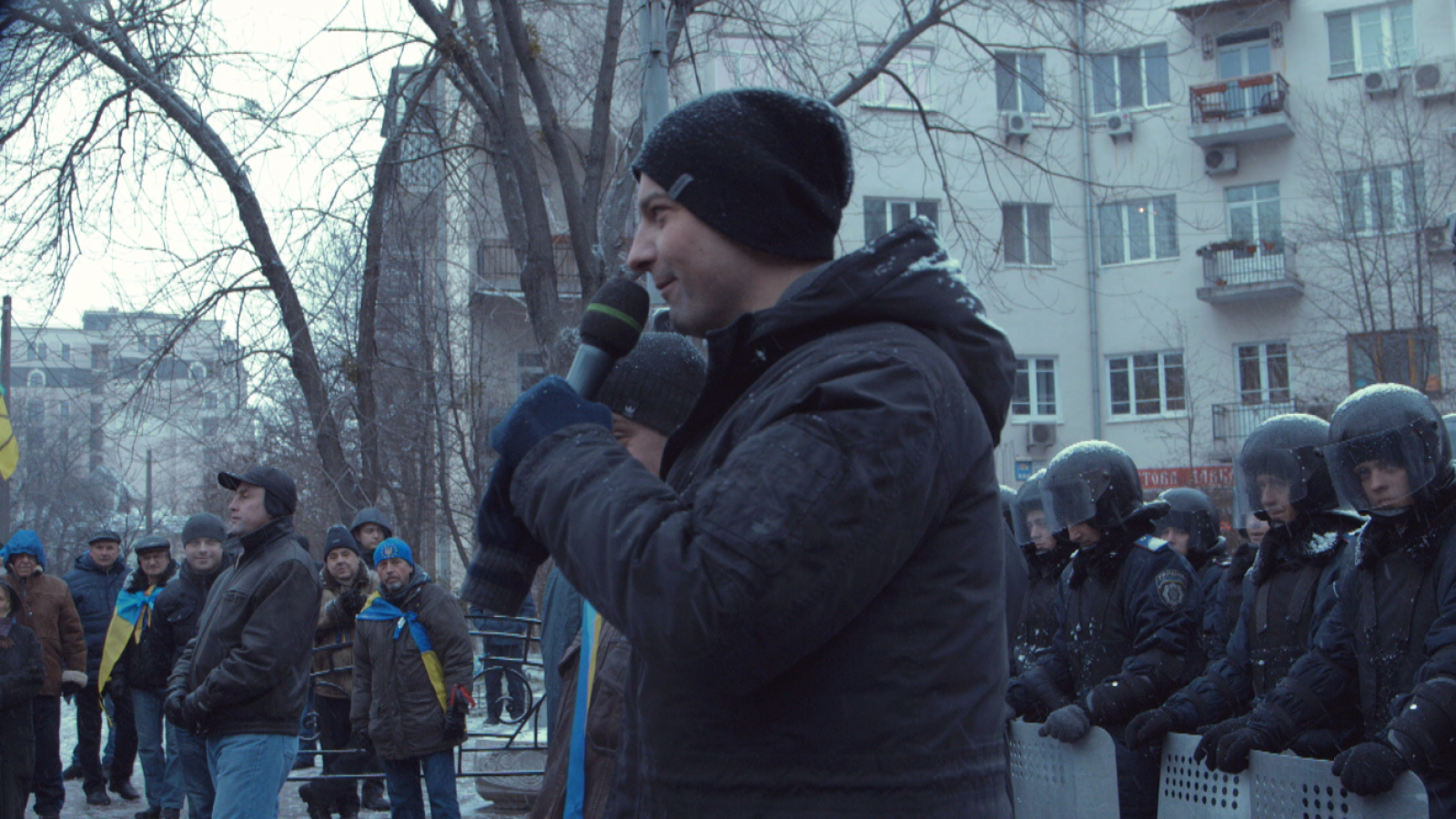 rus: Активіст з мікрофоном виступає перед публікою.