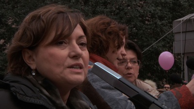 Mature brown-haired woman speaks into a microphone on the background of other women