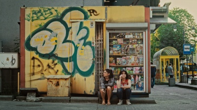 Two women are sitting near a kiosk.