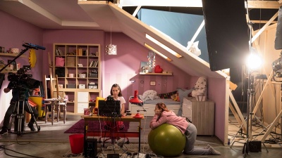 The girls look at a monitor in a pavilion-like room.