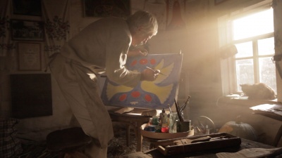 літній чоловік із пензлем у руці стоїть біля полотна малює картину. На ній зображено двох птахів.