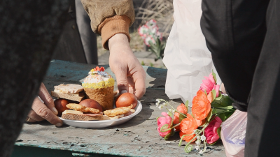 Hands lower a plate with Easter cake, Easter eggs and cookies next to a bouquet of plastic flowers